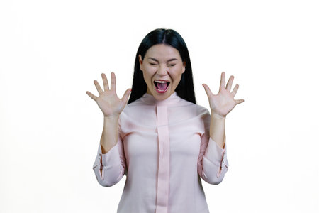 Young brunette asian woman is screaming out loud. Korean girl with her hands up. Isolated on white background.の写真素材