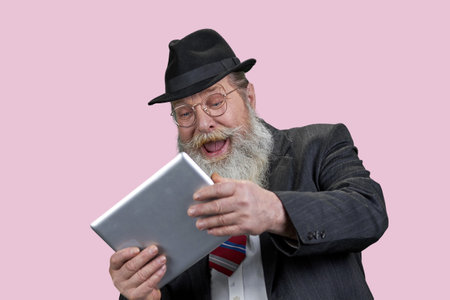 Portrait of laughing aged senior man with tablet pc. Happy grandpa with modern gadget. Isolated n pink.の写真素材