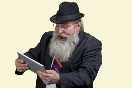 Portrait of excited senior man with tablet pc. Isolated on yellow.の写真素材