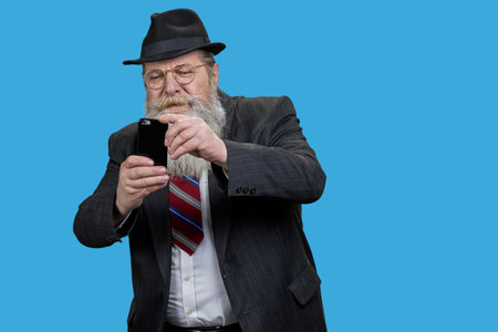 Portrait of bearded man focused on smartphone internet surf. Sends text messages in social networks. Isolated on blue.の写真素材