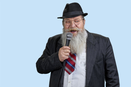 Portrait of excited aged man with microphone. Isolated on blue. Giving a speech.の写真素材