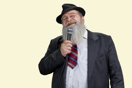 Portrait of aged bearded man singing with microphone. Isolated on pastel yellow background.の写真素材