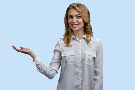 Happy blonde young female smiling and showing copy space. Pastel blue background.の写真素材