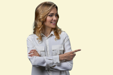 Portrait of a blonde female pointing to the right at copy space. Isolated on pastel yellow background.の写真素材