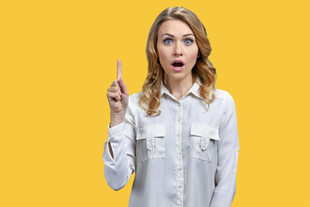 Young blue-eyed blonde woman is pointing up. Isolated on orange background.の写真素材
