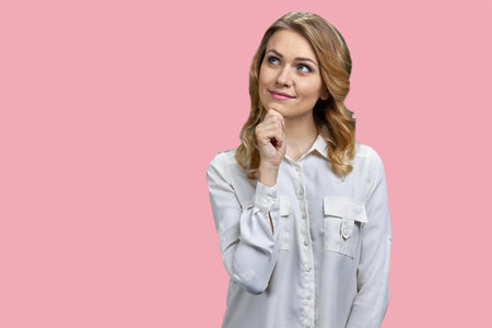 Portrait of a young thoughtful blonde woman touching her chin. Isolated on pink background.の写真素材