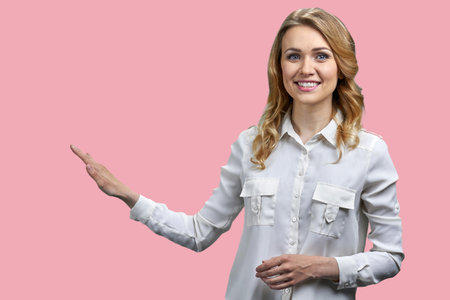 Happy young attractive woman pointing at copy space with her right hand. Isolated on pink background.の写真素材