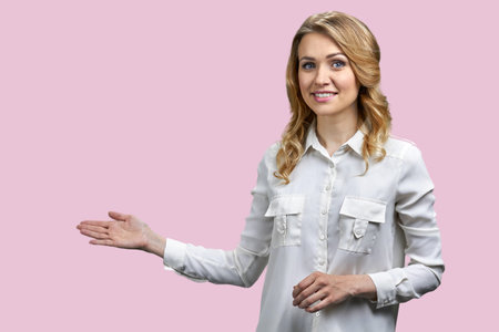 Portrait of a young blonde woman pointing at copy space with her right hand. Isolated on pink background.の写真素材