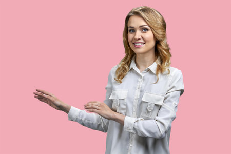 Attractive young blonde woman pointing at copy space with both hands. Isolated on pink background.の写真素材