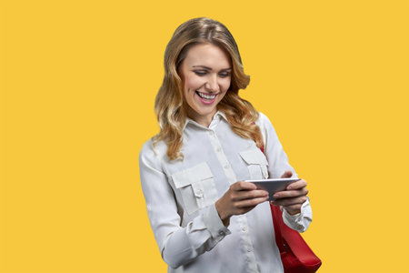 Young happy woman playing video game on her smartphone. Isolated on vivid yellow background.の写真素材