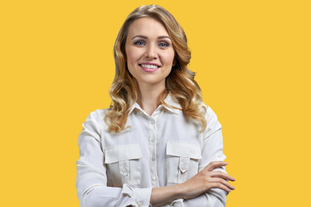 Protrait of a young blonde smiling woman with folded arms. Vivid yellow background.の写真素材