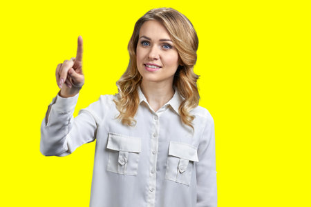 Portrait of blond woman is touching transparent virtual screen. Vivid yellow background.の写真素材