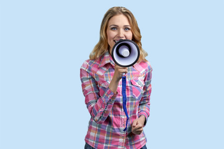 Young blonde blue-eyed woman holding a megaphone. Isolated on pastel blue background.の写真素材