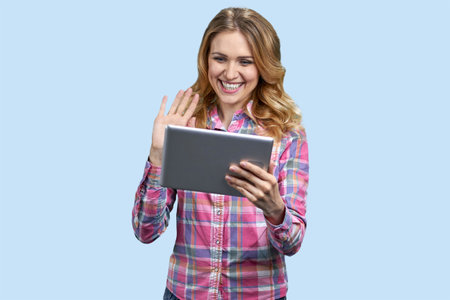 Portrait of blonde woman waving her hand to someone on tablet pc. Isolated on pastel blue.の写真素材