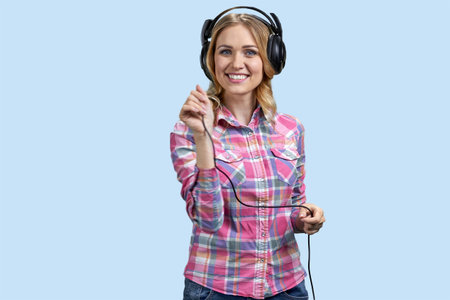 Portrait of young blonde cheerful woman wearing headphones. Isolated on pastel blue.の写真素材