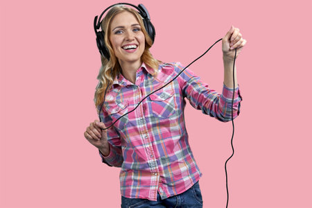 Young woman wearing headphones and holding the cord. Isolated on pink background.の写真素材