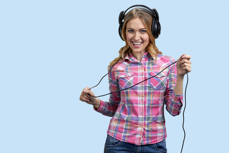 Portrait of young pretty woman wearing headphones and holding the cord. Isolated on pastel blue backgorund.の写真素材