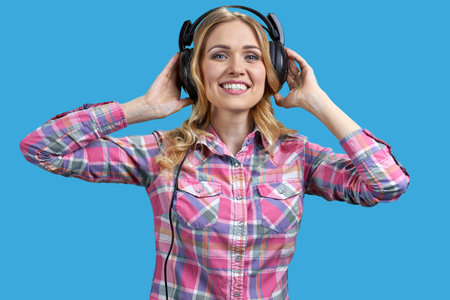 Attractive young blond woman wearing headphones and holding it with both hands. Isolated on vivid blue background.の写真素材