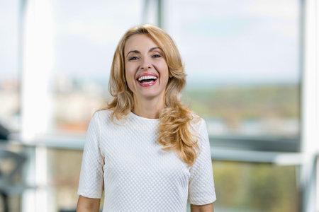 Portrait of blonde smiling laughing middle aged woman. Indoor window in the background.の写真素材