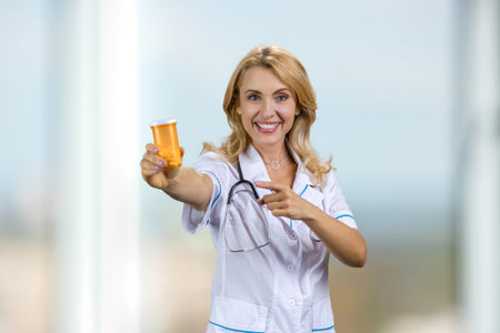 Happy blonde doctor advertising medicine bottle. Pointing at pills.の写真素材