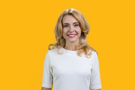 Happy mature blond woman in a white blouse. Isolated on orange.の写真素材