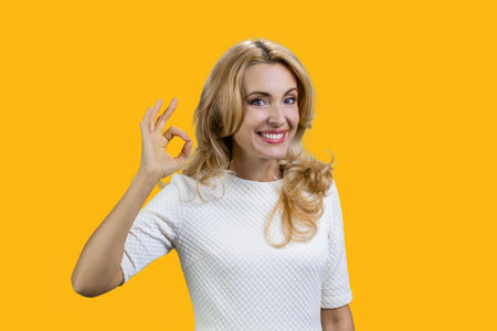 Portrait of a happy mature blond woman shows ok gesture sign. Isolated on orange.の写真素材