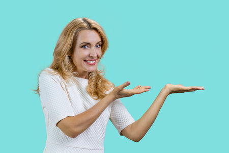 Portrait of a mature caucasian woman presenting copy space with both hands. Isolated on turquoise.の写真素材