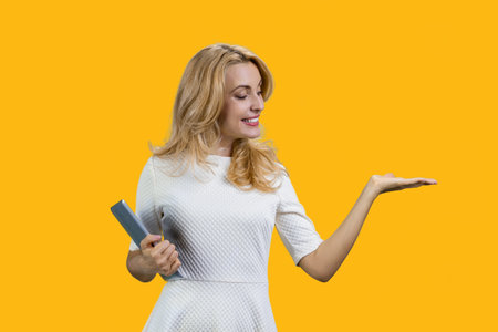 Happy caucasian woman holding a tablet device and showing copy space. Isolated on vivid yellow.の写真素材