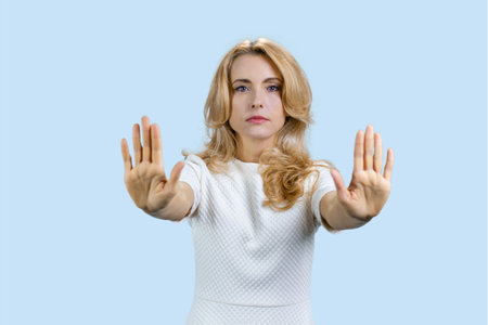 Portrait of caucasian mature woman shows stop sign prohibition with both hands. Isolated on pale blue.の写真素材