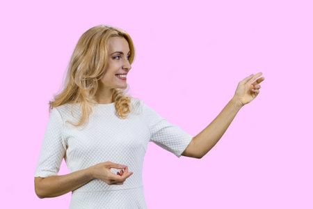 Happy mature blonde woman pointing at copy space. Isolated on pink.の写真素材