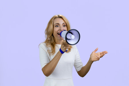 Happy positive blonde woman giving a speech in megaphone. Isolated on purple.の写真素材