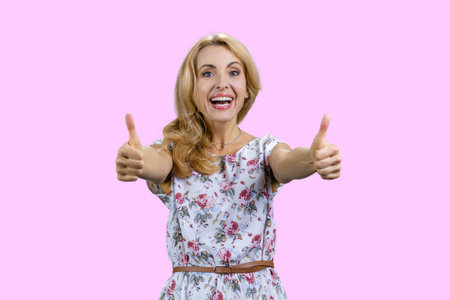 Happy young caucasian female gives both thumbs up. Isolated on pink.の写真素材