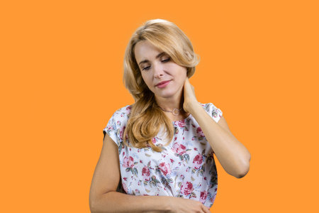 Portrait of mature blonde woman suffers from neckache. Isolated on orange.の写真素材