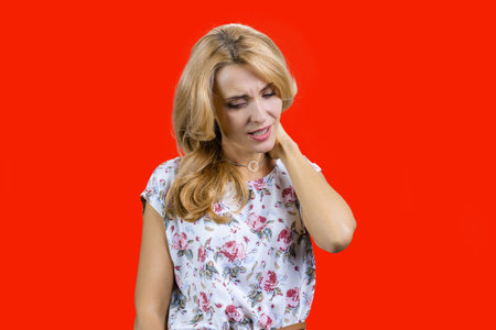 Portrait of middle middleaged caucasian blonde woman having a neck pain. Isolated on red.の写真素材