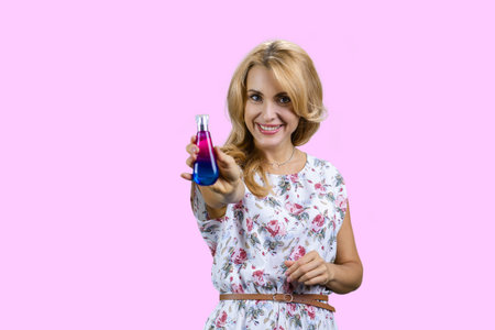 Portrait of happy mature blonde sprays fragrance on you. Isolated on pink.の写真素材