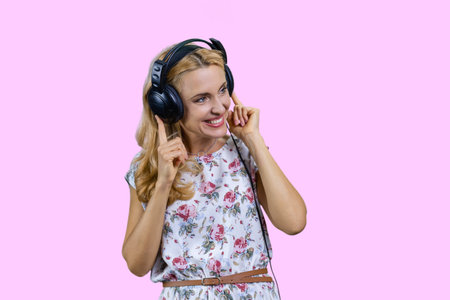 Blonde woman listening to music in headphones. Isolated on pink.の写真素材