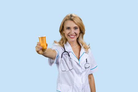 Portrait of happy caucasian female doctor giving an orange bottle of pills. Isolated on blue.の写真素材