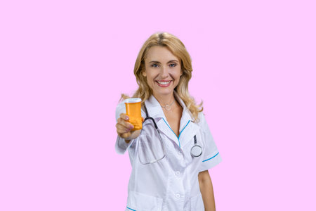 Portrait of professional caucasian female doctor giving an orange bottle of pills. Isolated on pink.の写真素材