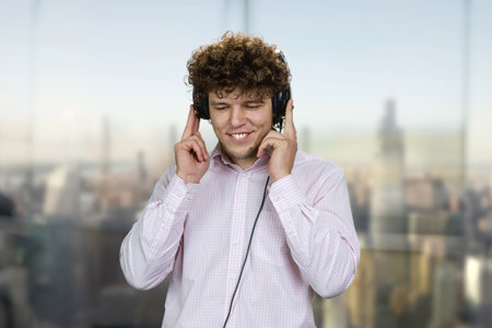 Happy young guy wearing headphones listening music. Blurred cityscape in the background.の写真素材