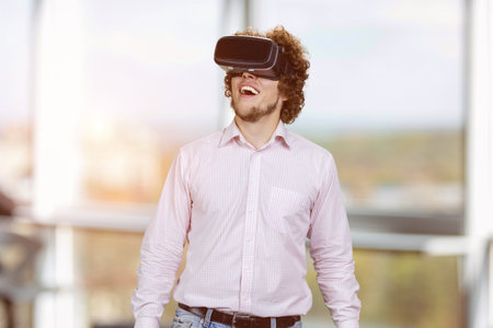 Portrait of young happy man with curly hair wearing vr headset. Indoor window in the background.の写真素材