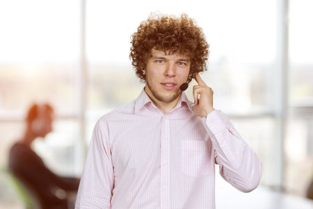 Young serious successful man in curly hair talking in microphone. Office interior in the background.の写真素材