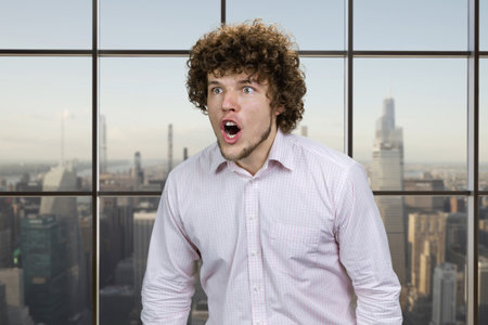 Young caucasian man with curly hair angrily screaming out loud. Checkered window with cityscape view in the background.の写真素材