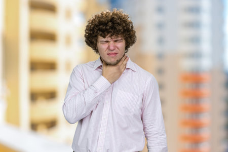 Young handsome man with curly hair touching his neck. Residential area buildings in the background.の写真素材