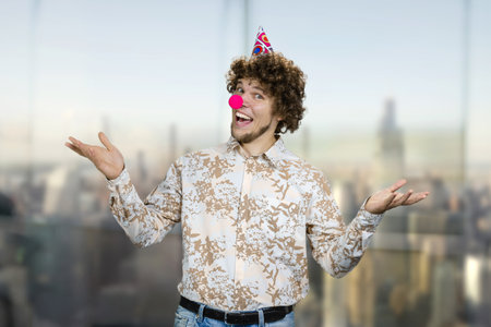 Portrait of a young caucasian guy with curly hair wearing a clowns nose. Happy birthday concept.の写真素材