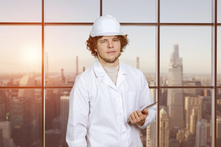 Portrait of a young guy in white uniform holding tablet pc device. Indoor window with cityscape view in the background.の写真素材