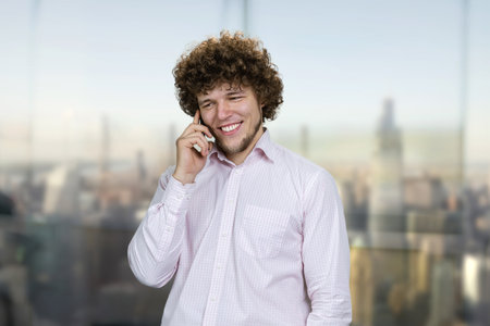 Portrait of a young caucasian man in white shirt talking on the phone. Urban cityscape in the background.の写真素材