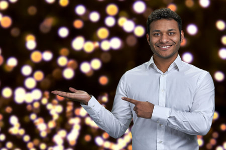 Handsome man looking at camera while presenting something on festive bokeh background. Christmas holiday deal.の写真素材