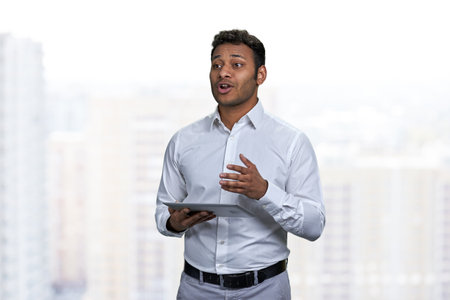 Speaking young manager using computer tablet while giving a presentation. Young indian businessman...