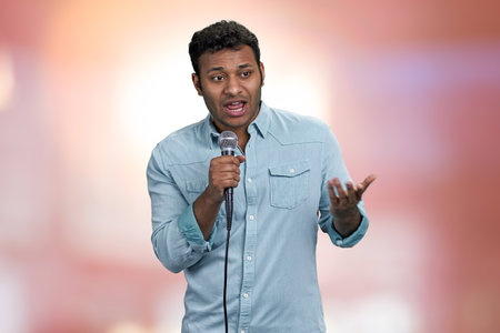 Young handsome man entertainer talking into microphone. Abstract pink bokeh background.の写真素材