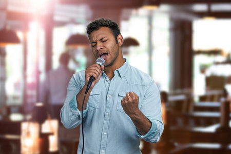 Enthusiastic young indian man performing song with microphone. Interior blur background.の写真素材